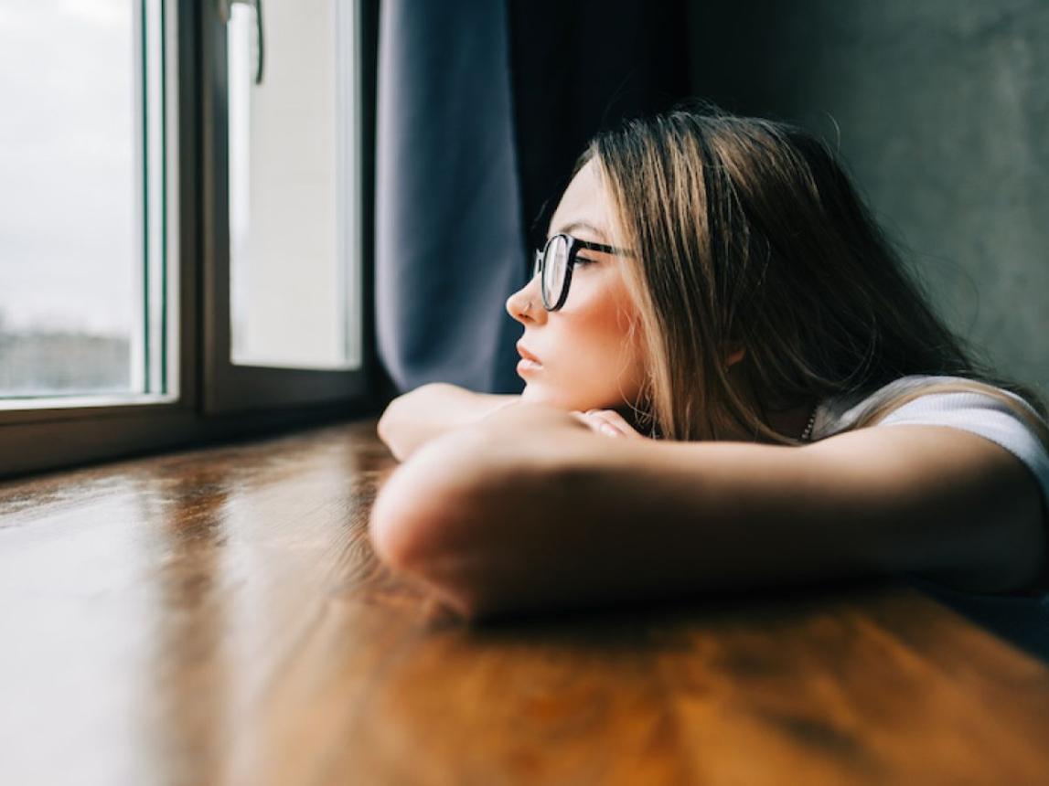 girl looking out window representing the weight of unfinished stories and unresolved feelings